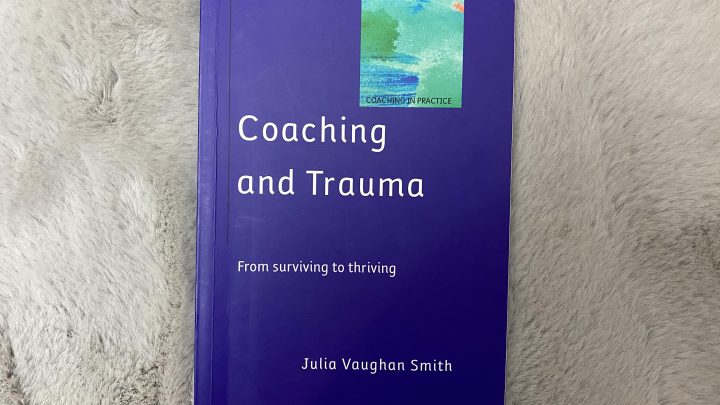 A blue book on a fluffy grey mat. titled Coaching and Trauma by Julia Vaughan-Smith